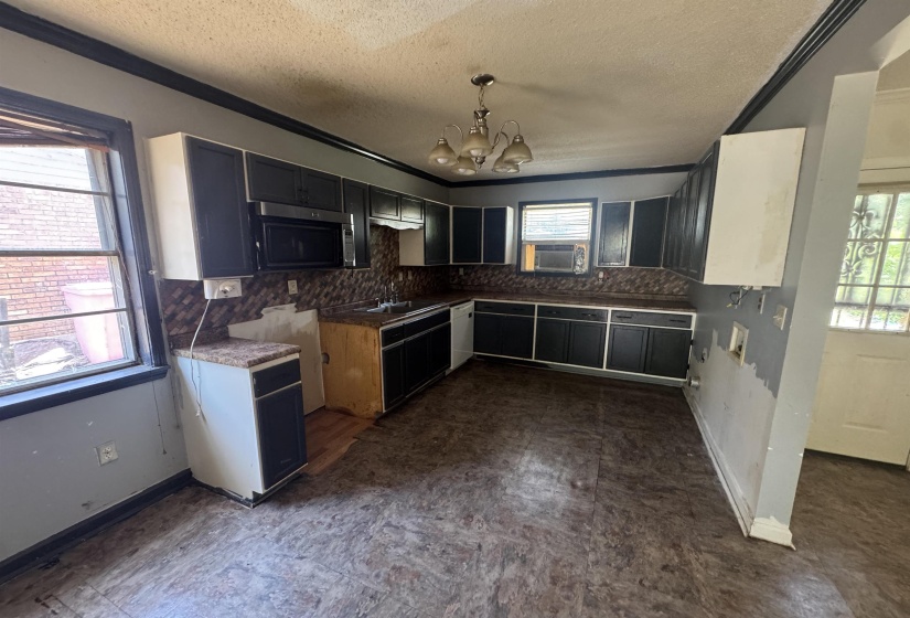 Kitchen featuring L-shaped cabinetry, built-in microwave, textured backsplash, and an overhead chandelier