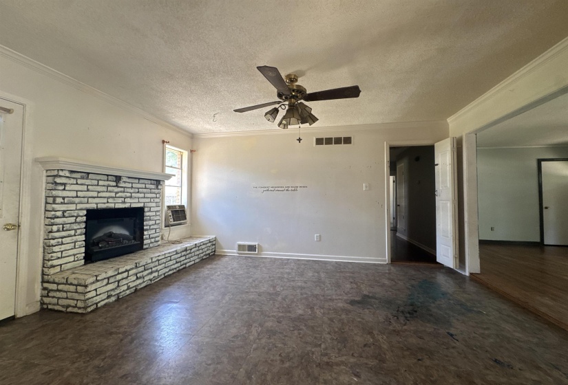 Spacious interior featuring a painted brick fireplace with a mantle, ceiling fan, and wood-finish flooring