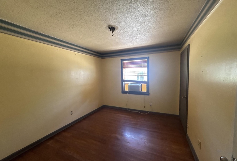 Room featuring wood-finish flooring, a window with horizontal blinds, and a dark-paneled door
