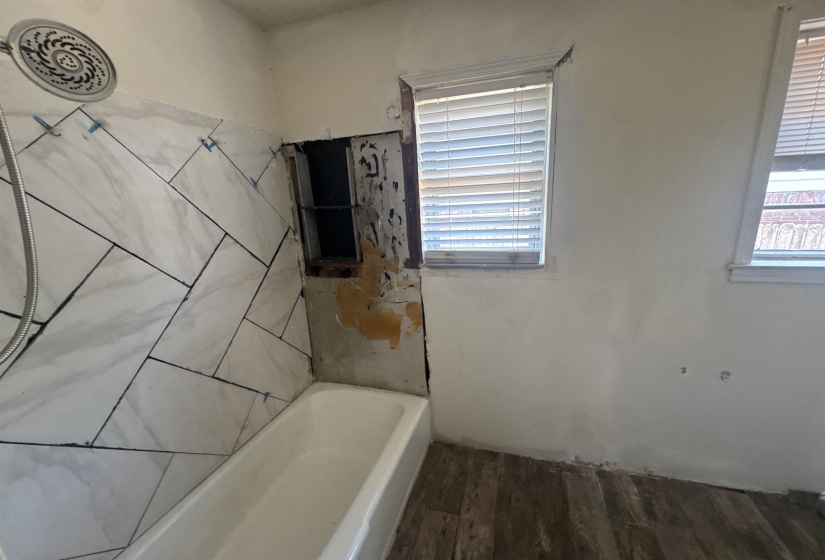 White bathtub featuring a partially tiled surround with a shower head fixture
