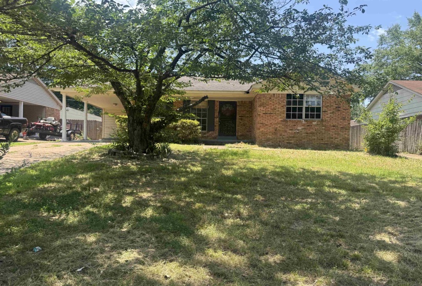 Brick exterior featuring a covered carport, mature front yard tree, and multi-pane windows