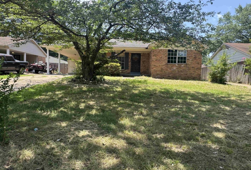 Brick facade home featuring a prominent mature tree, covered carport, and a partial privacy fence