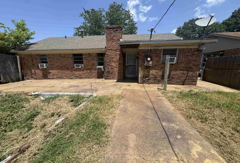 Brick exterior with multiple window units, a prominent brick chimney, and a concrete patio