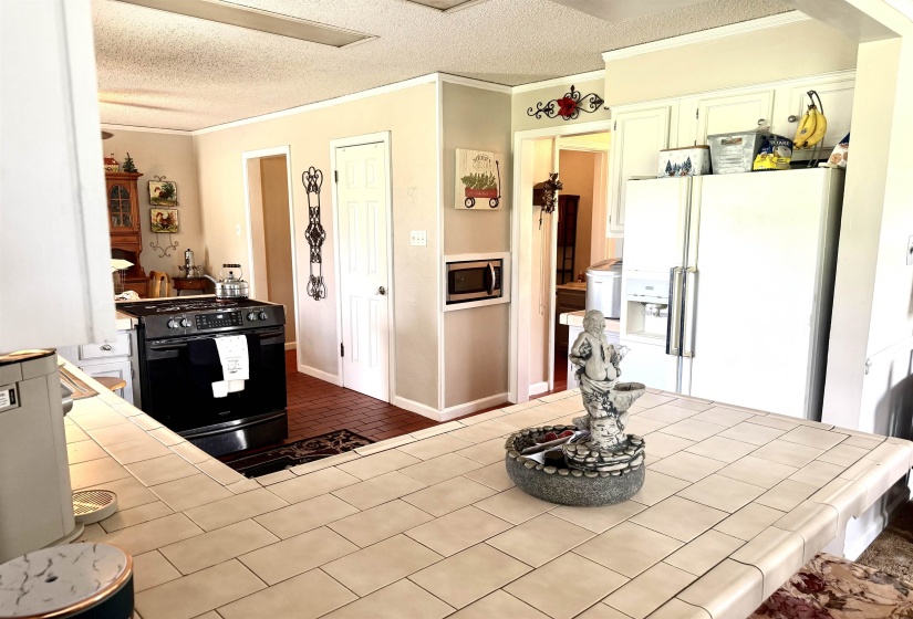Kitchen featuring tile countertops with rounded edges, white upper cabinetry, a freestanding black range, and a built-in microwave