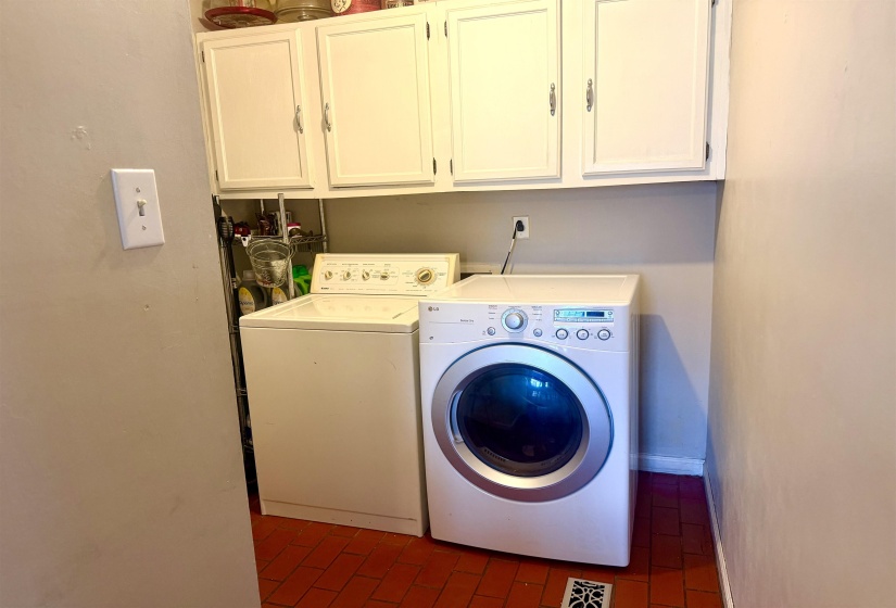 Laundry area featuring white upper cabinetry with silver hardware, red square tile flooring, and light-toned wall paint
