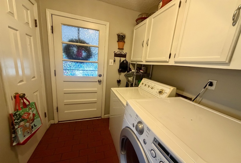 Utility room featuring red tile flooring and overhead white cabinetry