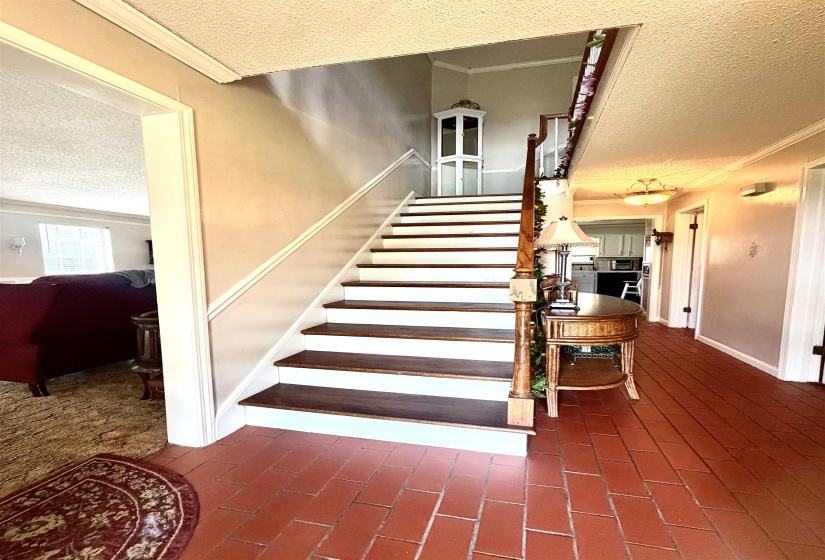 Entry foyer featuring a staircase with wood-finish treads and white risers, terracotta tile flooring, crown molding, and a chandelier-style light fixture
