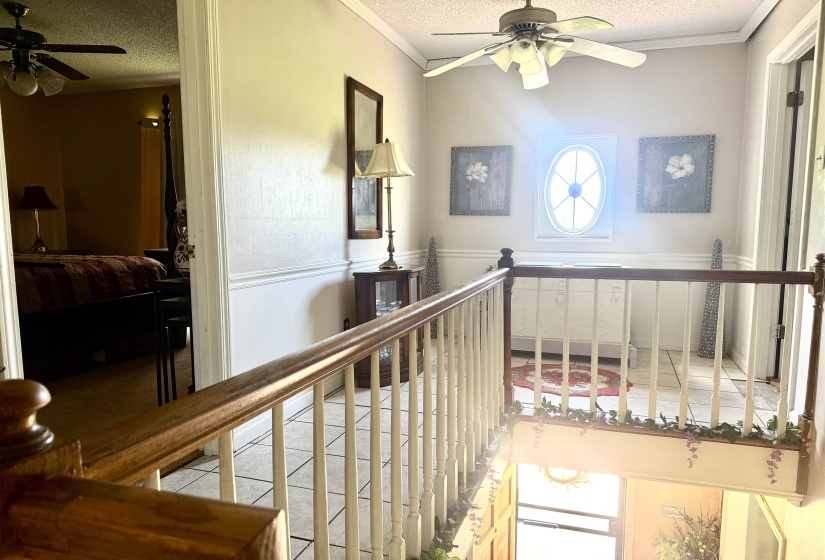 Upper-level landing featuring a wood-finish railing with white balusters, a ceiling fan, and an oval window