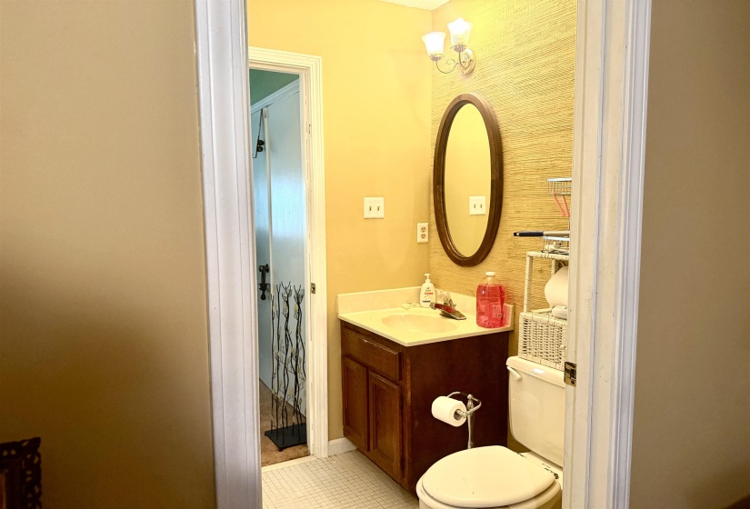 Compact bathroom featuring a dark wood-finish vanity with an integrated sink, an oval mirror, a two-light sconce, and textured wallpaper