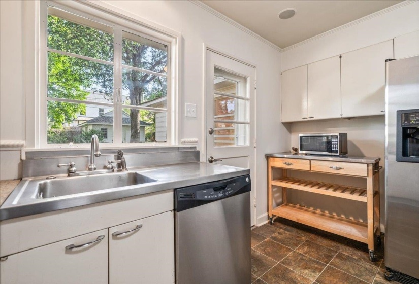 Kitchen featuring stainless steel appliances, stainless steel countertops, a deep basin sink, white cabinetry with silver hardware, and a glass-paneled door