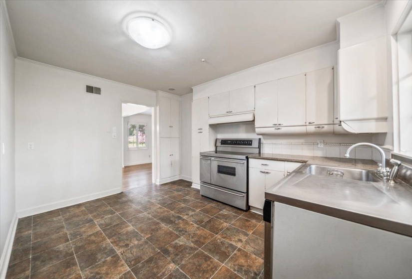 Kitchen featuring white cabinetry, stainless steel range and integrated sink, durable tile flooring, and a window for natural light