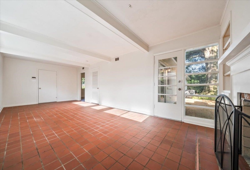 Spacious interior room featuring terra cotta tile flooring, white exposed ceiling beams, and a fireplace with a decorative metal screen