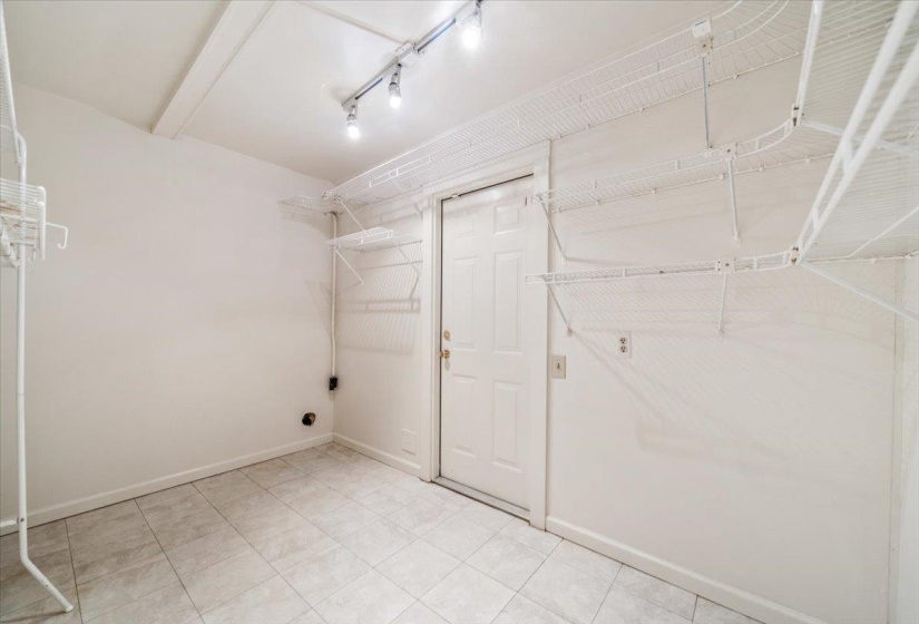 Utility room featuring tiled flooring, a white paneled door, track lighting, and built-in wire shelving