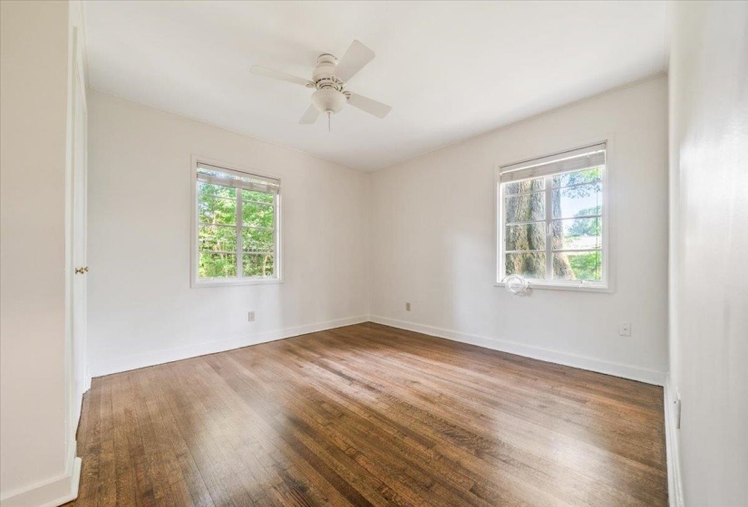 Bright room featuring wood-finish flooring, two window units, a white ceiling fan, and painted walls