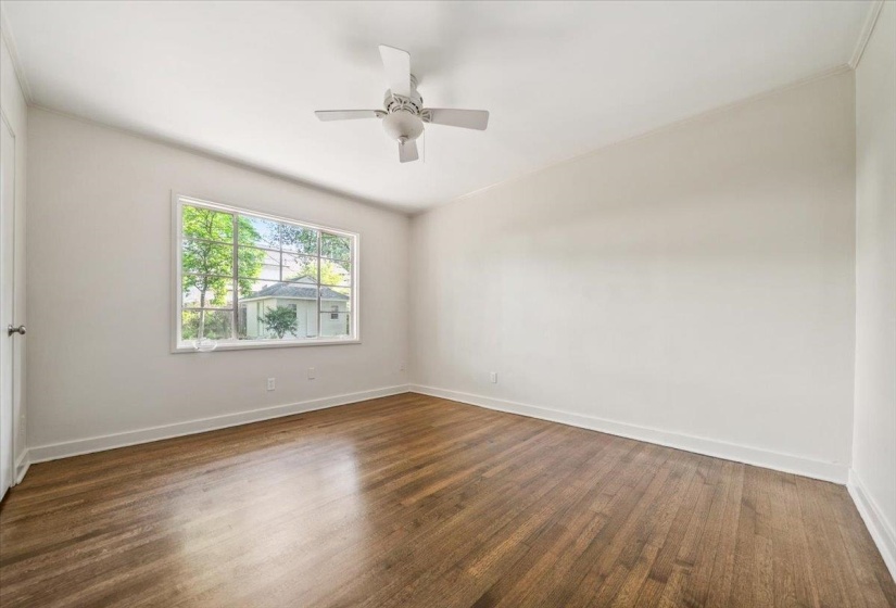 Bedroom featuring wood-finish flooring, a white ceiling fan, and a large window with white trim