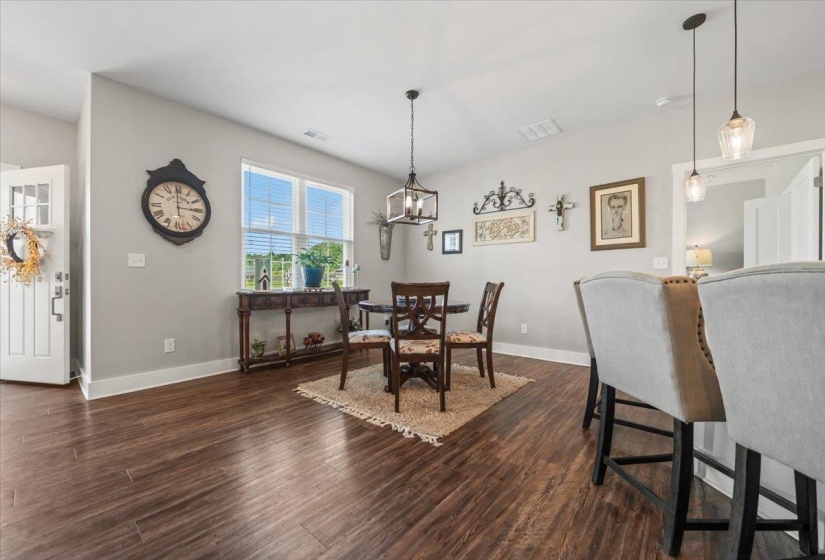 Open-concept living area featuring wood-finish flooring, a white paneled entry door with frosted glass, and a large window providing natural light