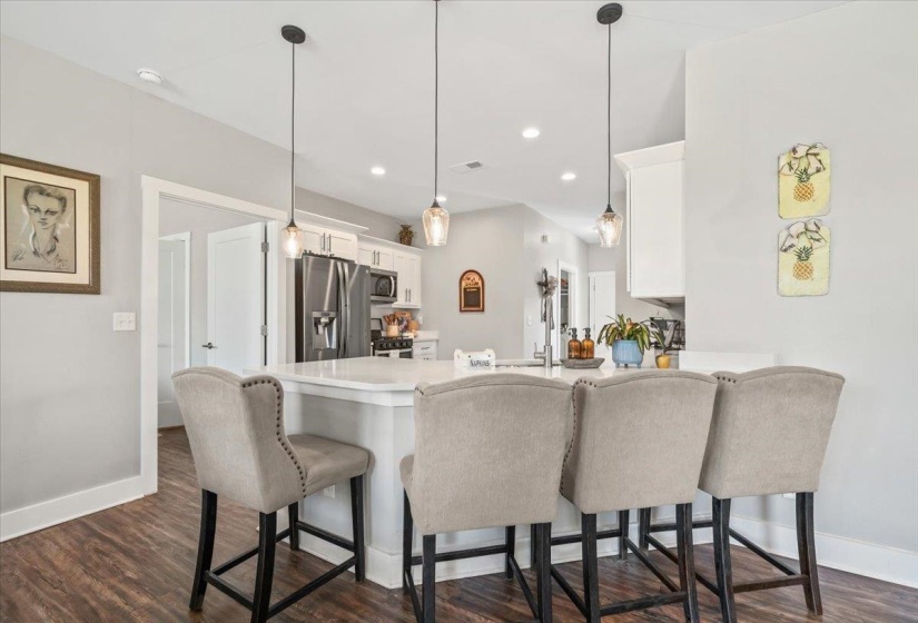 Open-concept kitchen featuring a white countertop island, pendant lighting, white cabinetry, stainless steel appliances, and wood-finish flooring