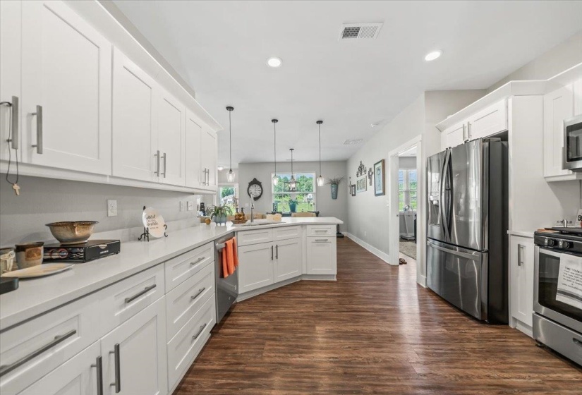 Modern kitchen featuring white cabinetry, light-toned countertops, stainless steel appliances, wood-finish flooring, and recessed lighting