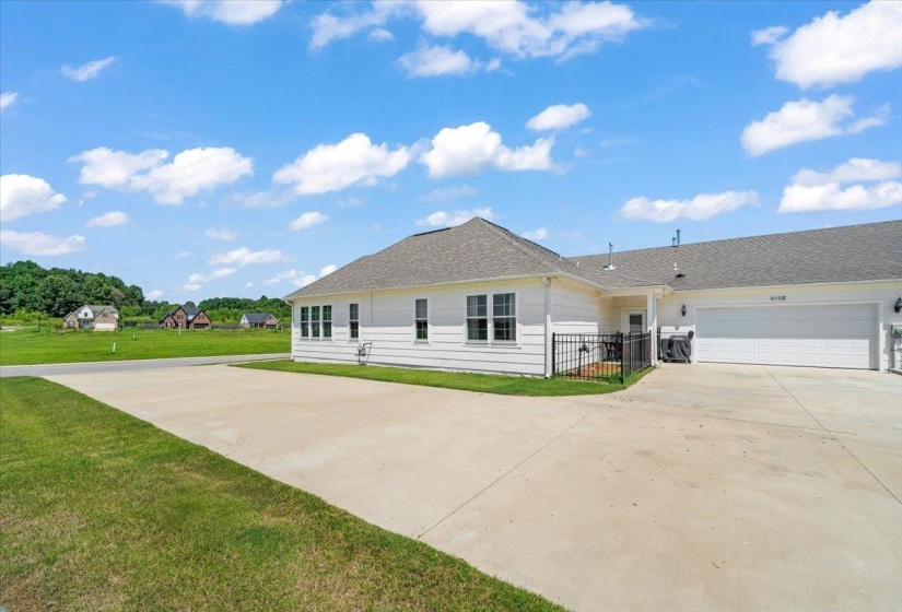 White siding exterior with multiple windows, a grey shingle roof, and a large concrete driveway