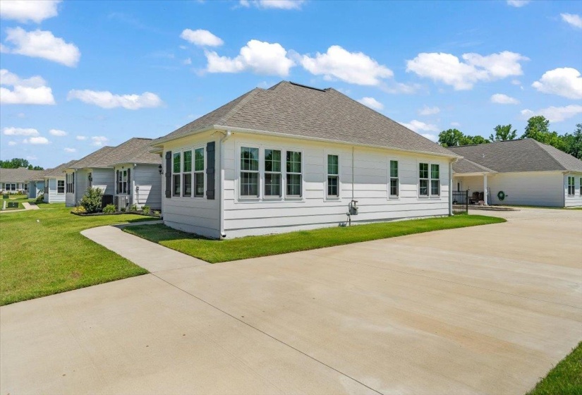 White-sided residence featuring a gray shingle roof, multiple windows with dark shutters, a concrete driveway, and a manicured lawn