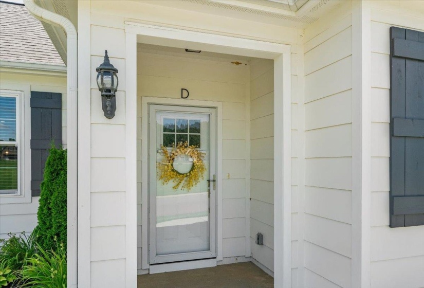 Front entry featuring a storm door, white siding, dark shutters, and an exterior wall lantern