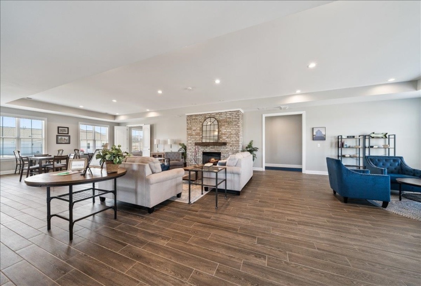 Expansive open-concept living area featuring wood-finish flooring, a brick fireplace with a mantel, recessed lighting, and multiple large windows