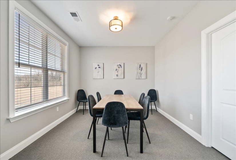 Carpeted room featuring a large window with blinds, a white paneled door, and a flush mount ceiling light