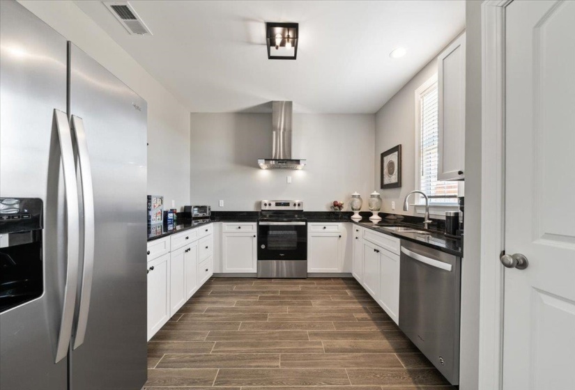 U-shaped kitchen featuring wood-finish flooring, white cabinetry, dark countertops, and stainless steel appliances including a refrigerator, range, and dishwasher