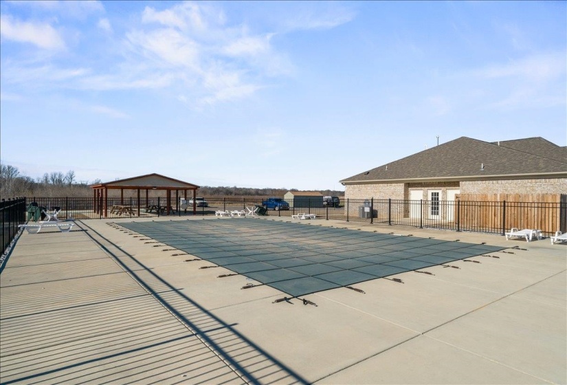 Expansive covered swimming pool with surrounding concrete decking, secured by black metal fencing