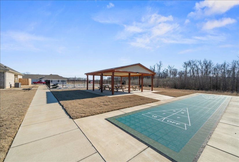 Outdoor recreation area featuring a shuffleboard court, covered pavilion with picnic tables, and concrete pathways