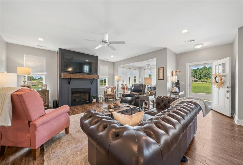 Spacious living area featuring wood-finish flooring, a contemporary fireplace with a dark surround and wooden mantel, recessed lighting, and a ceiling fan