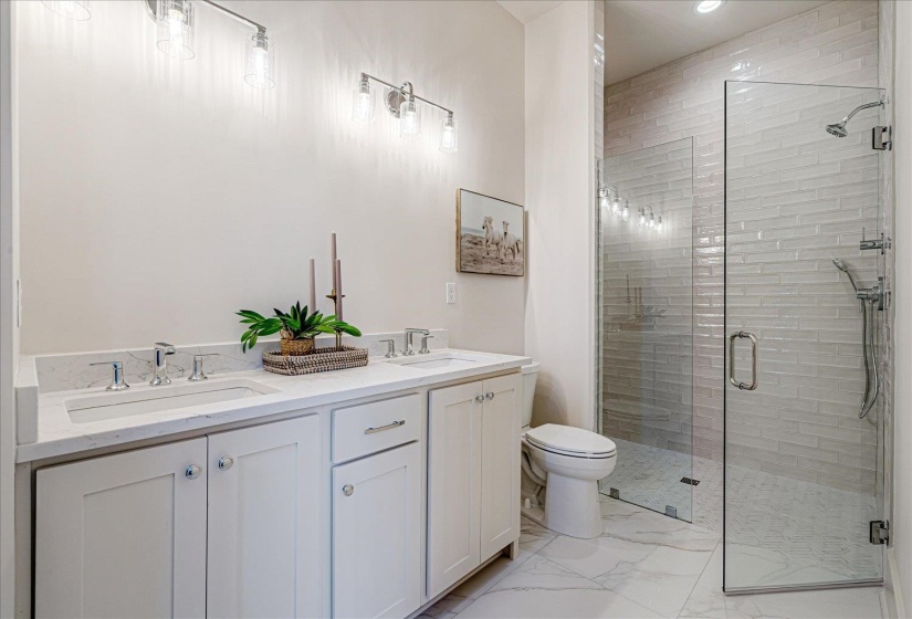 Full bath with double vanity, a shower stall, light marble finish flooring, and recessed lighting