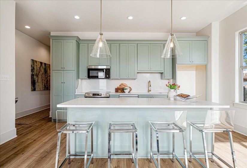 Kitchen featuring green cabinets, a kitchen bar, tasteful backsplash, stainless steel appliances, and decorative light fixtures