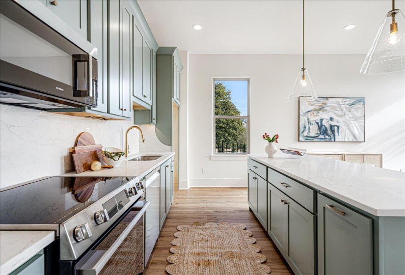 Kitchen featuring stainless steel appliances, light stone countertops, light wood-style flooring, a center island, and hanging light fixtures