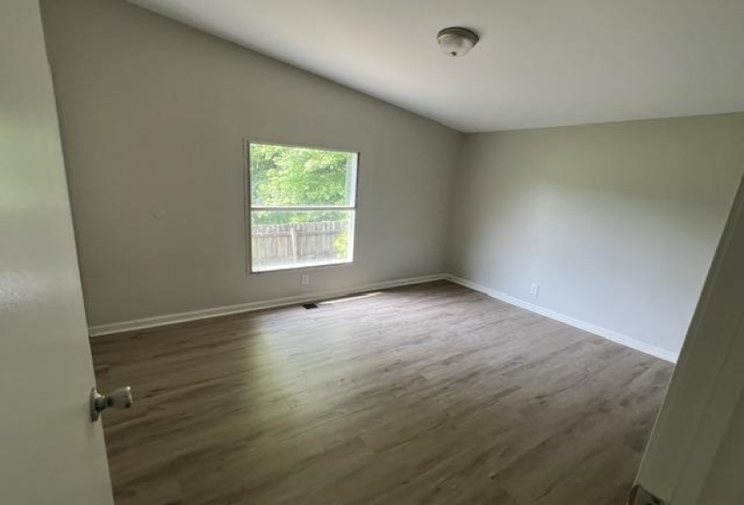 Room featuring wood-finish flooring, a vaulted ceiling, a single window, and a neutral wall color