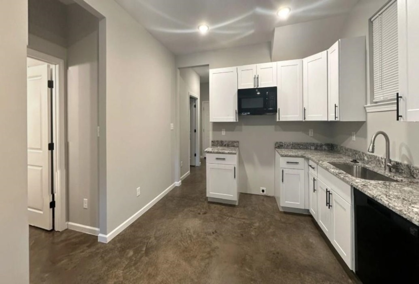 Kitchen featuring white cabinetry, concrete flooring, black appliances, and light stone countertops