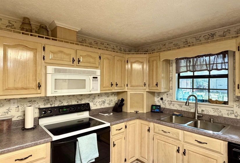 Kitchen featuring wood-finish cabinetry, built-in microwave, stainless steel double basin sink, black electric range, and light-toned countertops