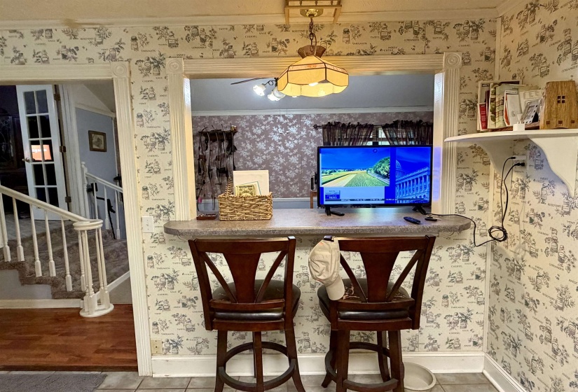 Kitchen pass-through window with a built-in counter bar, featuring a pendant light fixture, wall-mounted shelving, and patterned wallpaper