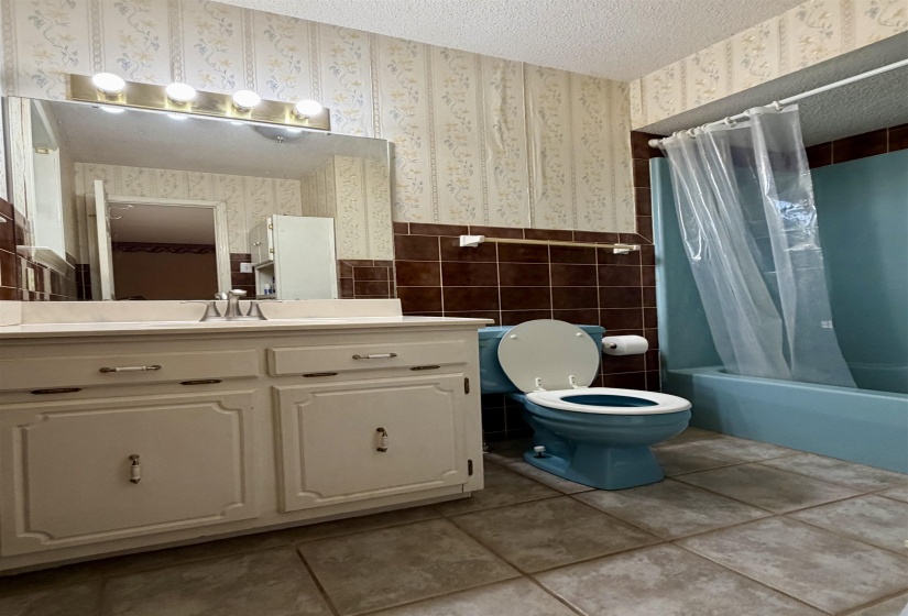 Bathroom featuring a vanity with integrated sink, a built-in mirror, overhead vanity lighting, a full-size bathtub, and tile flooring