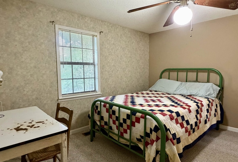 Bedroom featuring a window with blinds, textured wallpaper, neutral painted walls, carpeted flooring, and a ceiling fan with light fixture