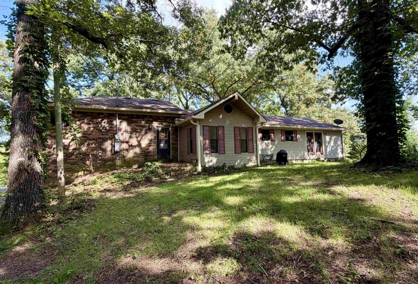 Exterior residential property featuring a combination of brick and siding finishes, a pitched roof, and mature trees providing natural shade