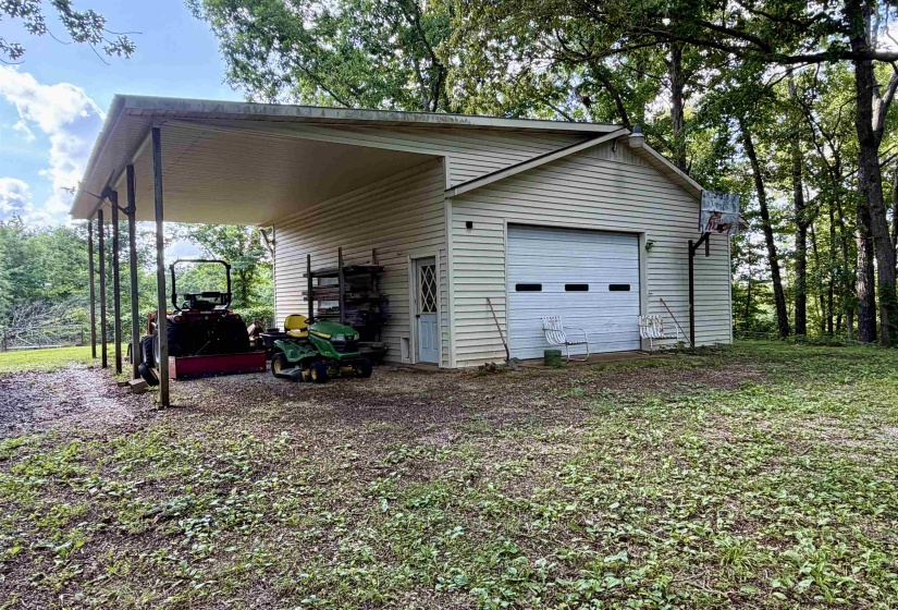 Detached auxiliary structure featuring horizontal siding, an overhead garage door, a covered carport, and a side entry door
