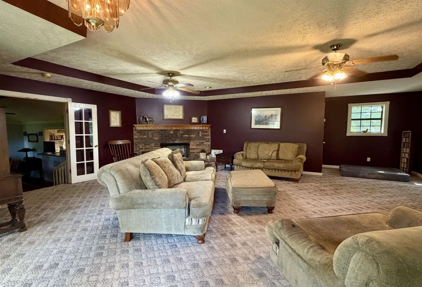 Spacious living area featuring patterned carpeting, a brick fireplace, and multiple ceiling fans