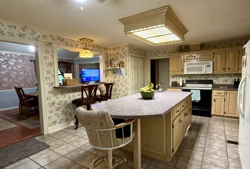 Kitchen featuring a center island with bar seating, overhead fluorescent lighting, wood-finish cabinetry, built-in microwave, and tile flooring