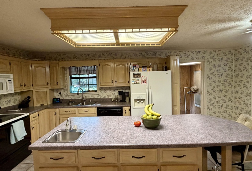 Kitchen featuring light wood cabinetry, a central island with an integrated sink, laminate countertops, and a built-in electric stove