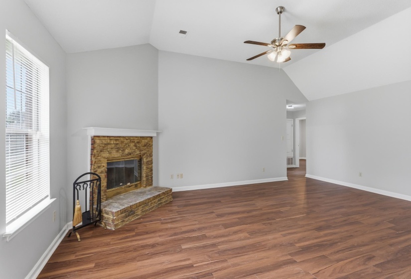 Living area featuring a brick-surround fireplace with a white mantel, high vaulted ceilings, wood-finish flooring, and a ceiling fan with light fixture