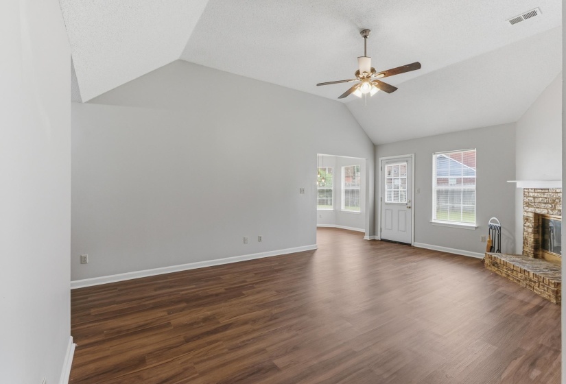 Spacious room featuring vaulted ceilings, wood-finish flooring, a ceiling fan with integrated lighting, and a brick fireplace