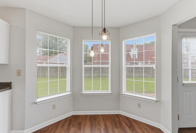 Bay window area featuring three large windows with white blinds, wood-finish flooring, and two modern pendant light fixtures