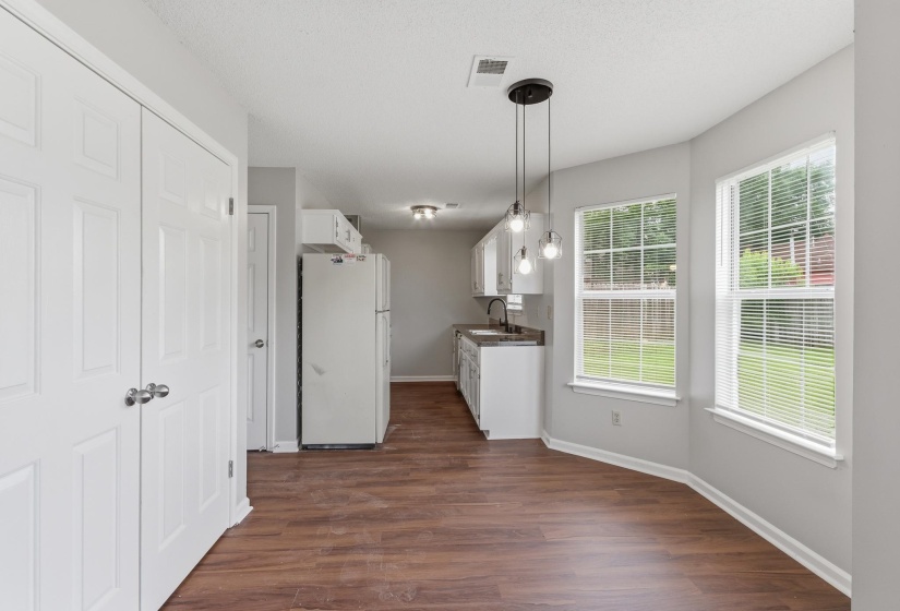 Open concept kitchen and dining area featuring wood-finish flooring, white cabinetry, a modern pendant light fixture, and multiple windows