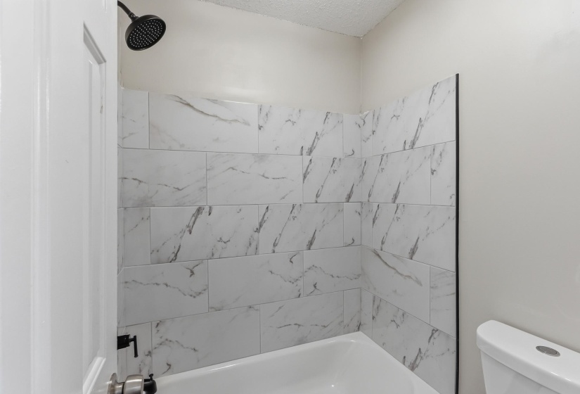 Bathtub with subway-style white tile surround featuring grey veining